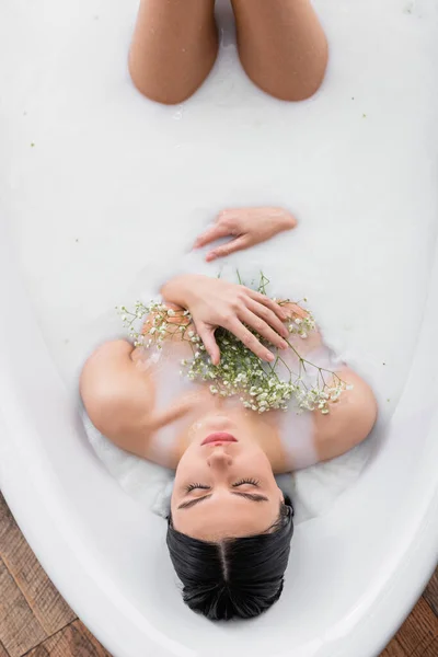 Vue aérienne de jolie femme aux fleurs de gypsophila appréciant se baigner dans le lait — Photo de stock