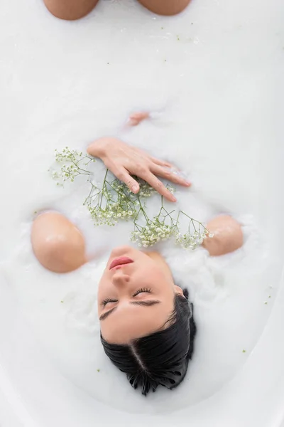 Overhead view of sensual woman with white, tiny flowers relaxing in milk bath — Stock Photo