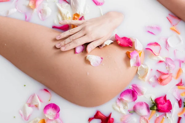 Partial view of young woman enjoying bathing in milk with rose petals — Stock Photo