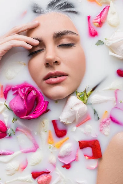 Bella donna toccare il viso durante il bagno nel latte con petali di rosa — Foto stock