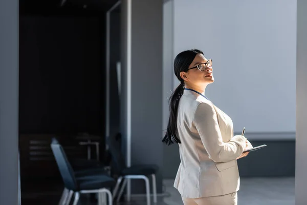 Smiling asian businesswoman holding notebook and pen in office — Stock Photo