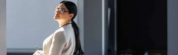 Smiling asian businesswoman in formal wear holding pen in office, banner — Stock Photo