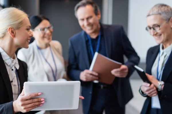 Digital tablet in hand of businesswoman near blurred colleagues — Stock Photo