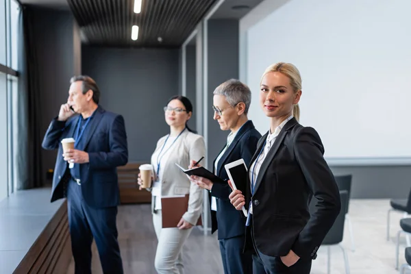 Businesswoman with digital tablet looking at camera near colleagues on blurred background — Stock Photo