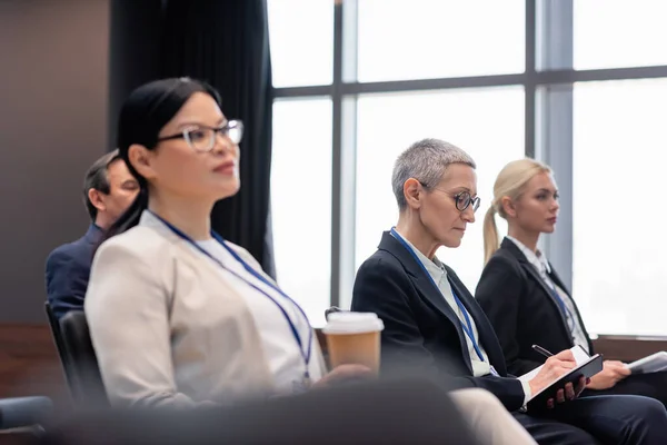 Femme d'affaires écrivant sur ordinateur portable près de collègues interraciaux dans la salle de conférence — Photo de stock