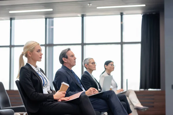 Businesswoman with paper folder and coffee to go sitting in conference room — Stock Photo