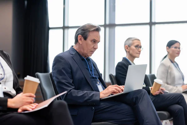 Uomo d'affari che utilizza laptop vicino ai colleghi durante il seminario — Foto stock