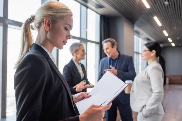 Side view of businesswoman looking at papers near blurred colleagues — Stock Photo