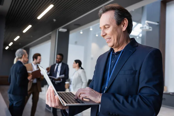 Smiling businessman using laptop in office hall — Stock Photo