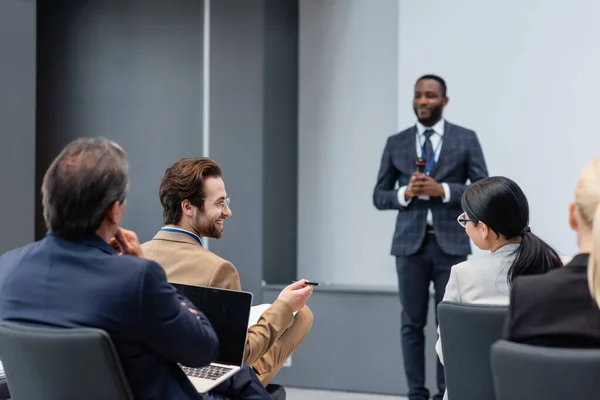 Улыбающийся бизнесмен разговаривает с коллегой, едва не размытым африканским оратором в конференц-зале — стоковое фото