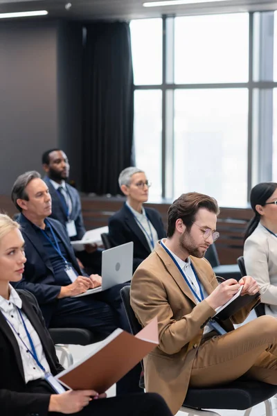 Uomo d'affari che scrive sul taccuino durante il seminario in sala conferenze — Foto stock