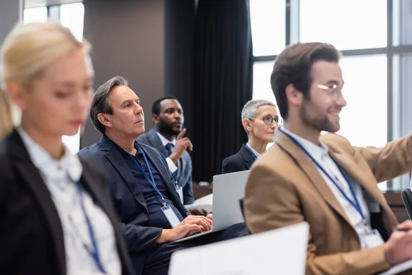 Empresário maduro usando laptop durante seminário perto de pessoas de negócios inter-raciais — Fotografia de Stock