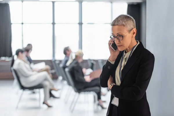 Donna d'affari matura che parla su smartphone vicino alla sala conferenze — Foto stock