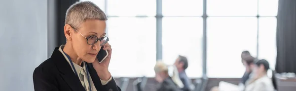 Зріла бізнес-леді розмовляє на мобільному телефоні біля конференц-залу, банер — стокове фото