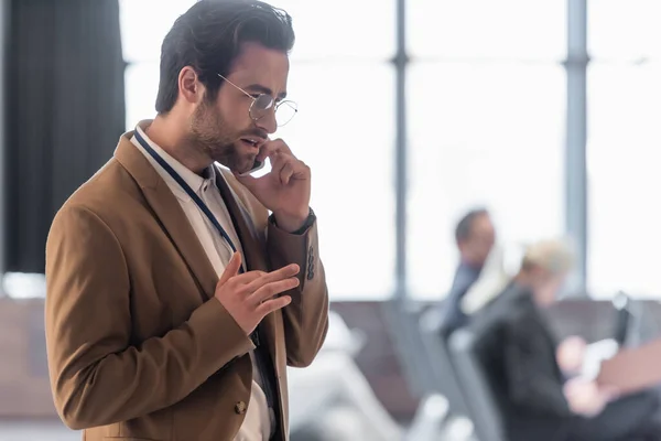 Young businessman talking on cellphone near blurred conference room — Stock Photo