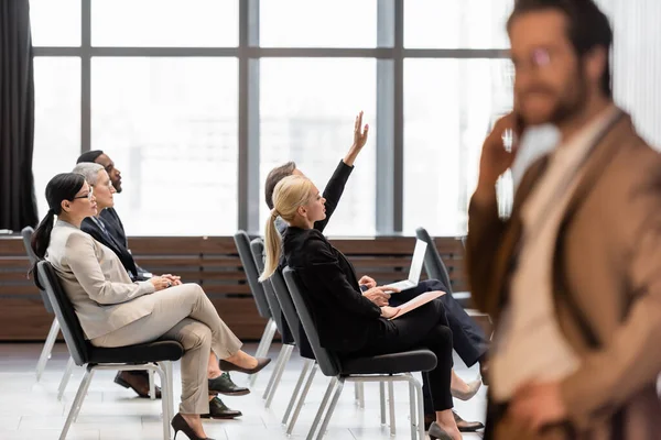 Interracial business people sitting in conference room near blurred businessman — Stock Photo