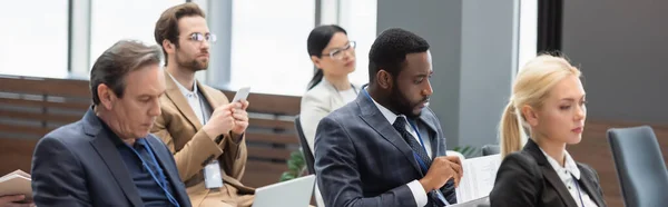 African american businessman looking at papers near colleagues in conference room, banner — Stock Photo