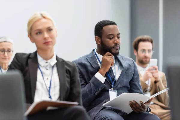 African american businessman looking at papers during seminar near colleagues — Stock Photo