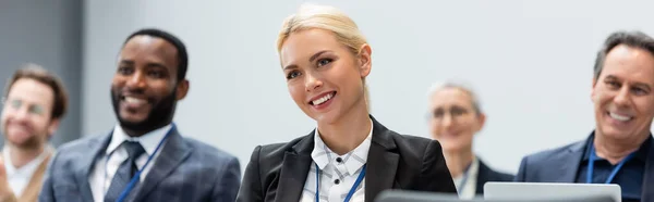 Donna d'affari sorridente che guarda altrove vicino a colleghi multietnici in sala conferenze, striscione — Foto stock