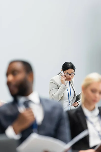 Mujer de negocios asiática con tableta digital hablando en smartphone durante el seminario - foto de stock