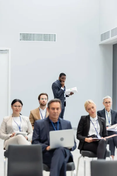 Homme d'affaires afro-américain tenant des documents près des hommes d'affaires interraciaux flous dans la salle de conférence — Photo de stock