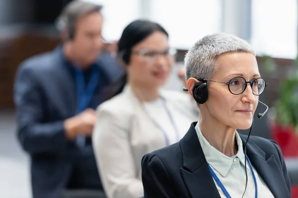 Зрелая деловая женщина в наушниках сидит в конференц-зале — стоковое фото
