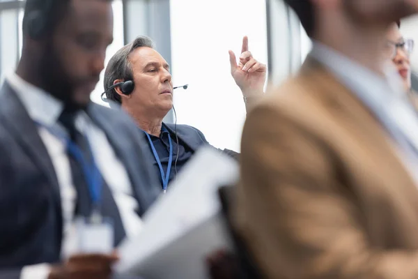 Mature businessman in headset talking during business conference — Stock Photo