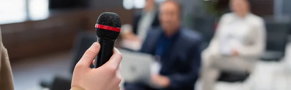 Lecturer holding microphone near blurred audience during seminar, banner — Stock Photo