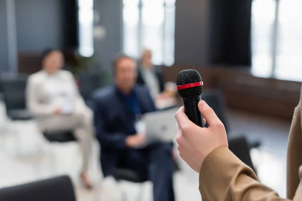 Redner hält Mikrofon in der Nähe verschwommener Teilnehmer während Geschäftskonferenz — Stockfoto
