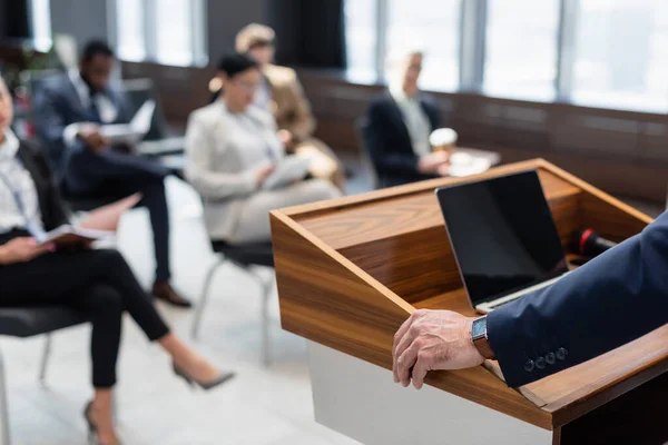 Foyer sélectif du conférencier près d'un ordinateur portable avec écran vierge et public interracial flou — Photo de stock