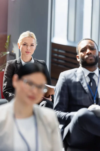 Enfoque selectivo de mujer de negocios rubia cerca de colegas interracial en primer plano borrosa - foto de stock