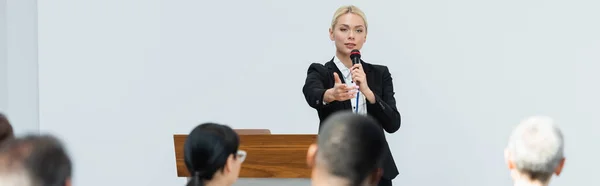 Altavoz rubia sosteniendo micrófono mientras señala a los participantes durante el seminario, pancarta - foto de stock