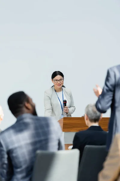 Espalda vista de borroso hombre de negocios haciendo pregunta a asiático altavoz durante conferencia - foto de stock