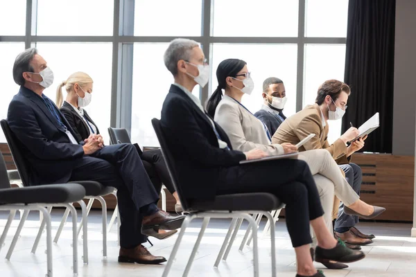 Gente de negocios multicultural con máscaras médicas sentados en la sala de conferencias durante el seminario - foto de stock