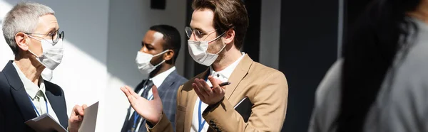 Young businessman in medical mask talking to mature colleague, banner — Stock Photo