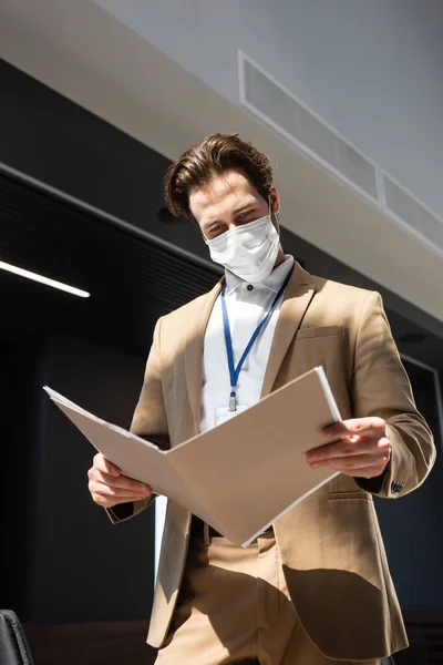 Jovem empresário em máscara médica olhando para documentos no escritório — Fotografia de Stock