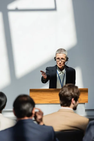 Vue arrière des gens d'affaires flous près du conférencier pointant de la main pendant la conférence — Photo de stock