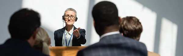 Middle aged speaker pointing at blurred business people during seminar, banner — Stock Photo