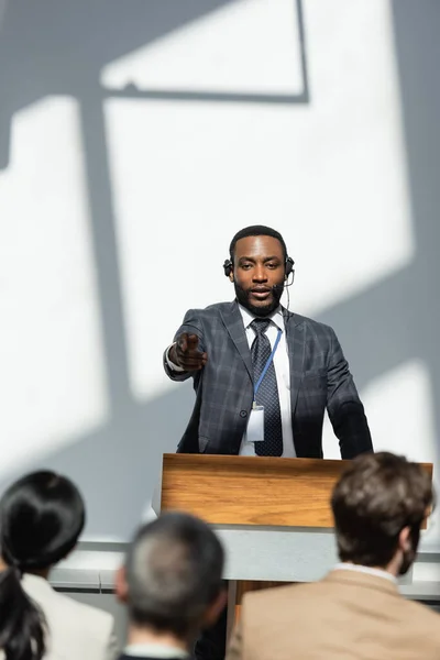 Conférencier afro-américain pointant vers le public sur le premier plan flou pendant le séminaire — Photo de stock