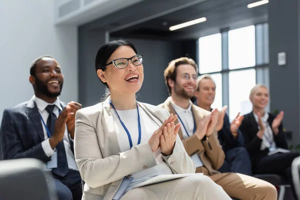 Asiatische Geschäftsfrau applaudiert während eines Seminars in der Nähe von verschwommenen interrassischen Kollegen — Stockfoto