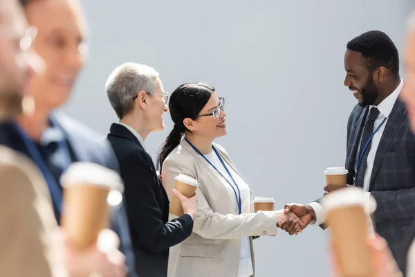 Enfoque selectivo de las personas de negocios multiétnicos estrechando las manos cerca de colegas durante el descanso del café - foto de stock