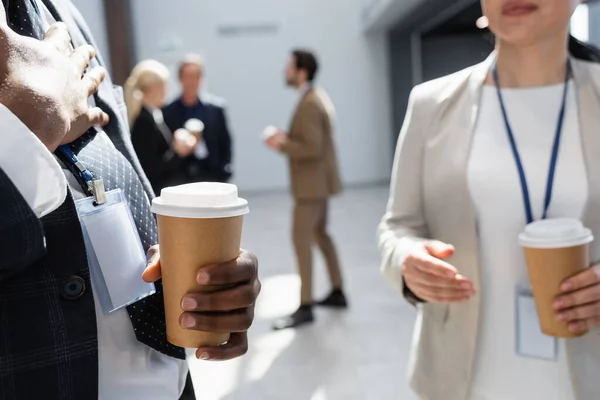 Africano americano empresário segurando café para ir perto de colegas em fundo turvo — Fotografia de Stock