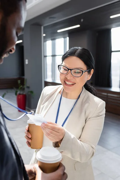 Cheerful asian businesswoman looking at id card of african american colleague — Stock Photo