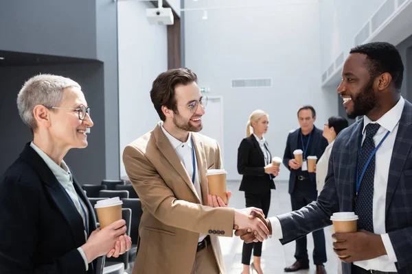 Colegas de negócios multiculturais felizes apertando as mãos durante o coffee break — Fotografia de Stock