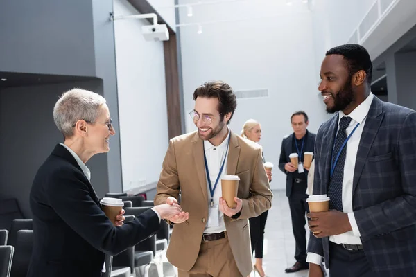 Young businessman shaking hand of mature businesswoman near african american colleague — Stock Photo