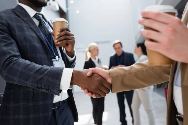 Hombres de negocios interracial estrechando las manos cerca de colegas en un fondo borroso - foto de stock