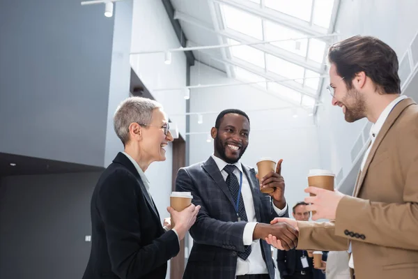 Happy african american businessman shaking hands with young colleague during coffee break — Stock Photo