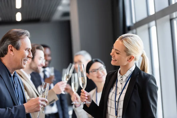 Smiling interracial business people holding champagne glasses during conversation in hall — Stock Photo