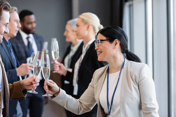 Feliz socio de negocios multiétnico tintineo copas de champán durante la conferencia - foto de stock