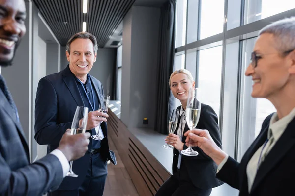 Sonrientes socios comerciales interraciales sosteniendo copas de champán mientras hablan en conferencia — Stock Photo